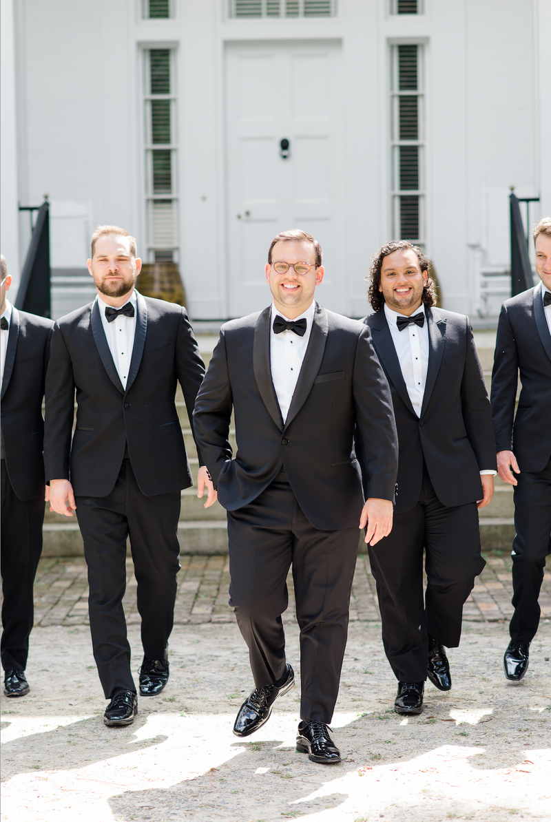 groomsmen in tux with wedding party behind